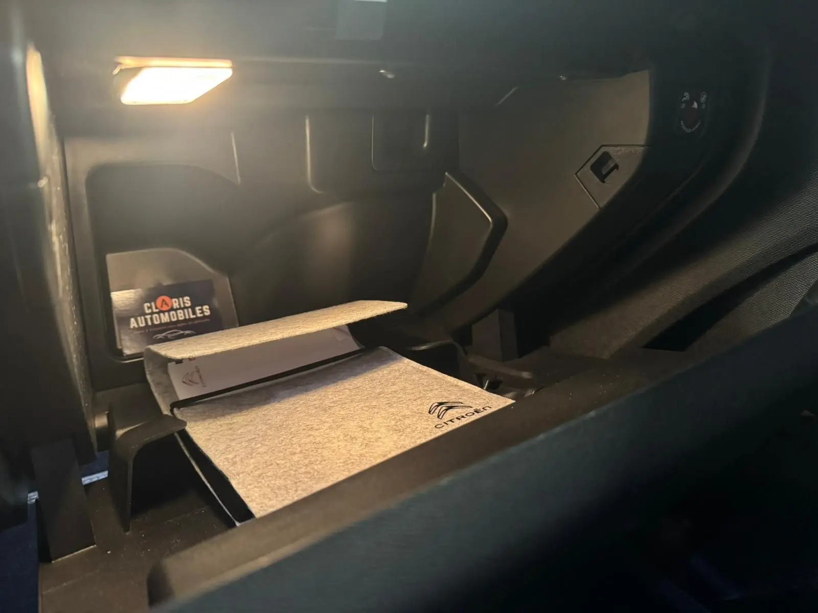 Vue intérieure du coffre à gants ouvert du Citroën C5 Aircross bleu avec manuel et éclairage intérieur allumé.