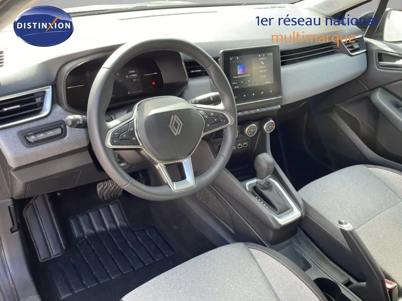 Vue intérieure côté conducteur de la Renault Clio 2025, volant cuir, tableau de bord gris et console centrale avec écran tactile.