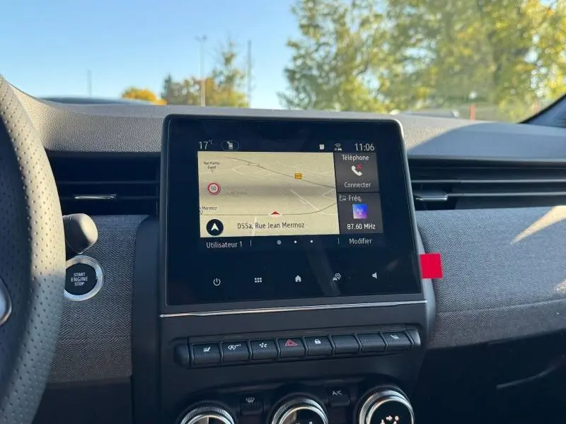 Vue intérieure centrée sur l’écran tactile multifonction de la Renault Clio orange 2025 avec tableau de bord texturé gris.