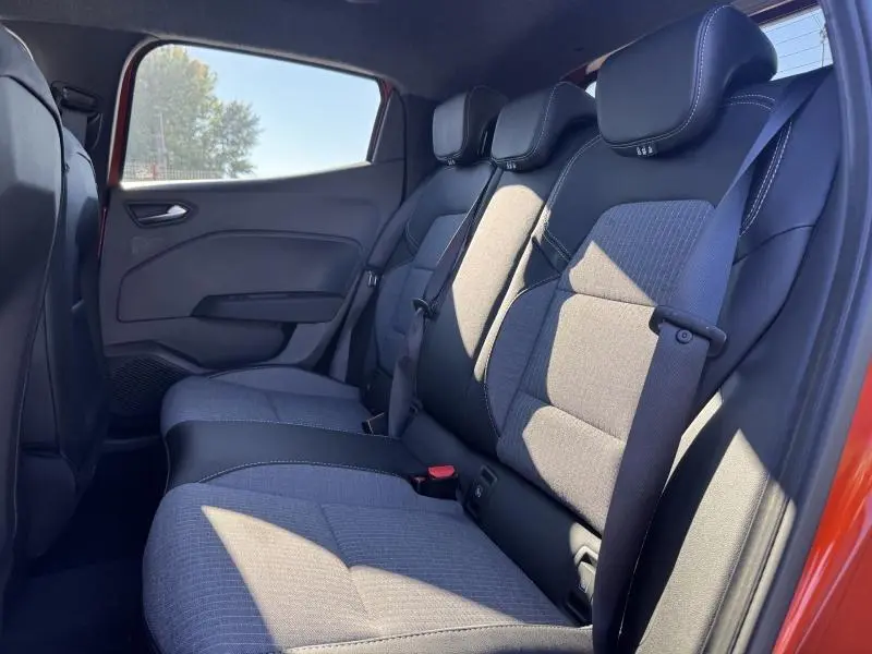 Vue latérale droite de l'habitacle arrière de la Renault Clio orange 2025, sièges tissu noir et gris avec ceintures de sécurité.