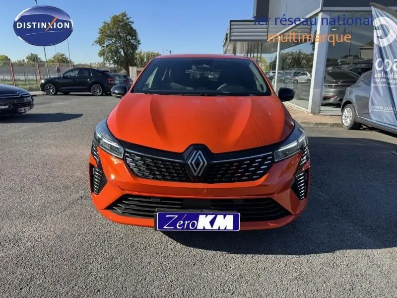 Vue avant d'une Renault Clio orange Valencia 2025 avec calandre noire et phares LED allumés.