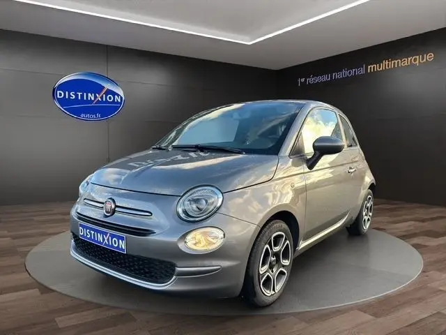 Vue 3/4 avant d'une FIAT 500 gris foncé avec jantes distinctives et phares ronds dans un showroom.
