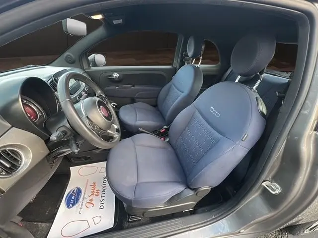 Vue intérieure côté conducteur d'une FIAT 500 gris foncé, sièges avant bleus avec logo 500 brodé sur appuie-tête.