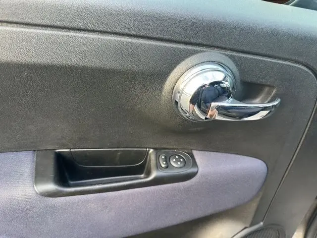 Poignée intérieure chromée côté gauche de la porte d’une FIAT 500 gris foncé, avec commandes électriques des rétroviseurs.
