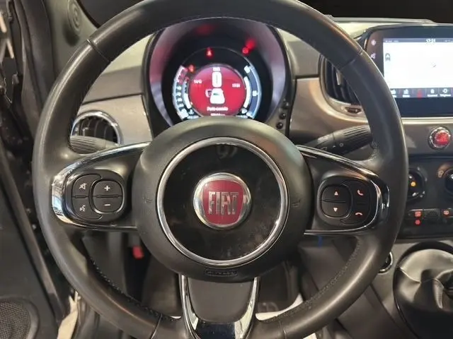 Vue rapprochée du volant cuir multifonctions noir de la FIAT 500 gris foncé avec tableau de bord et écran tactile visibles.