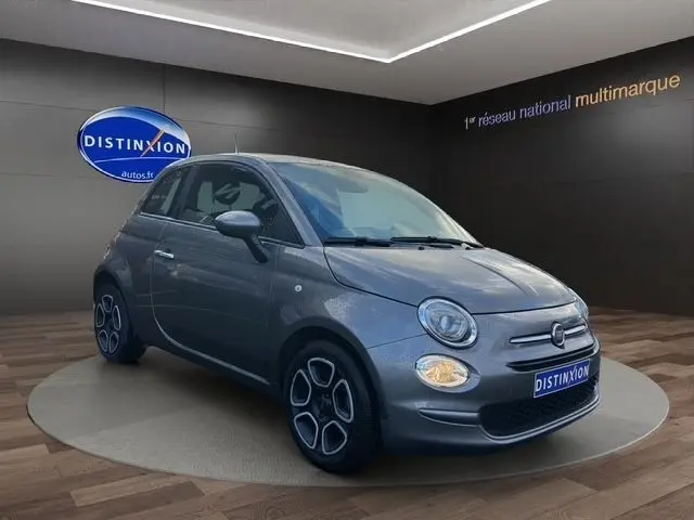 Vue 3/4 avant droite d'une Fiat 500 gris foncé avec phares ronds et jantes au design distinctif en concession.