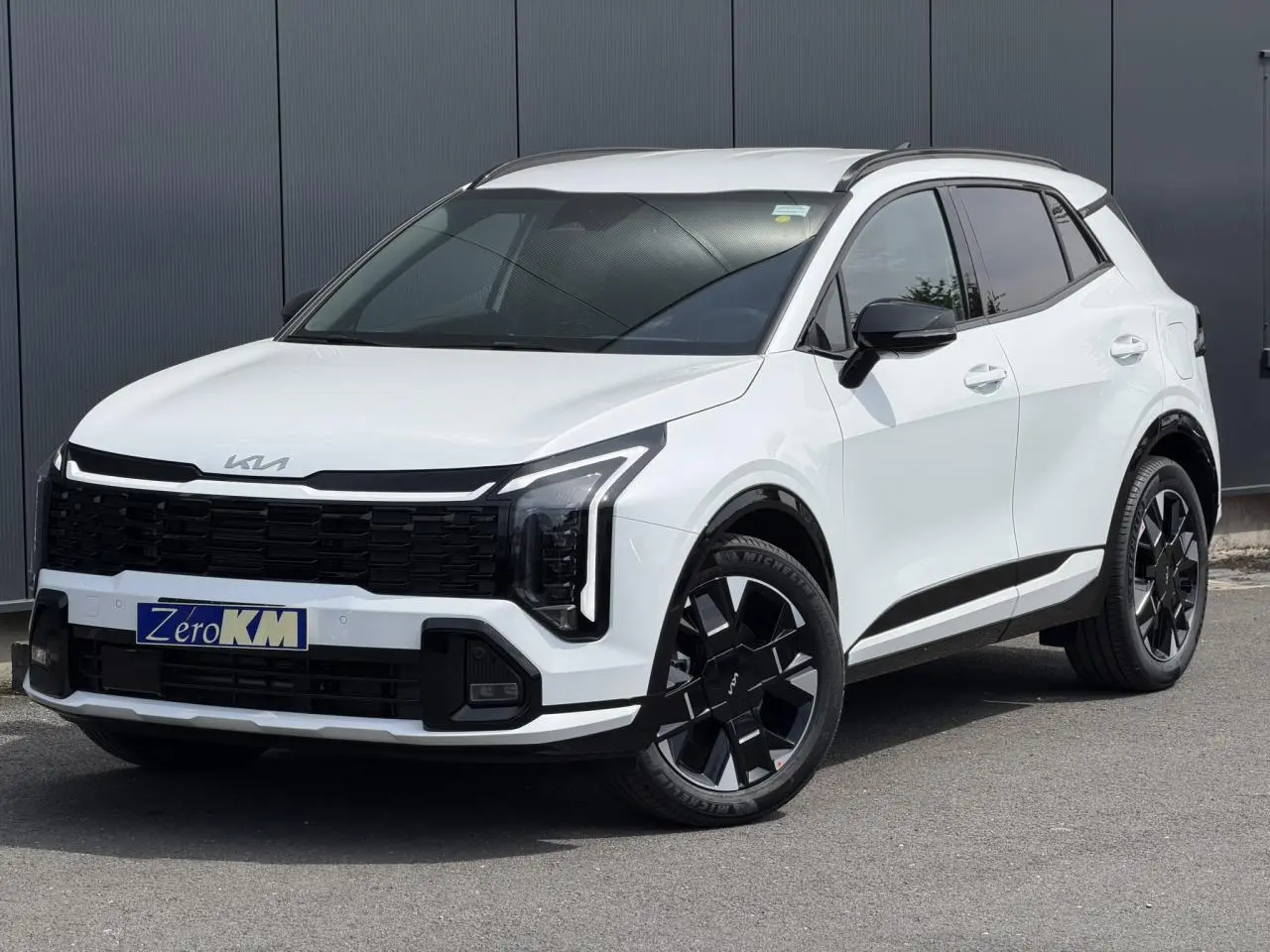 KIA SPORTAGE blanc en 3/4 avant droit, avec calandre noire et jantes alliage 19 pouces distinctives.
