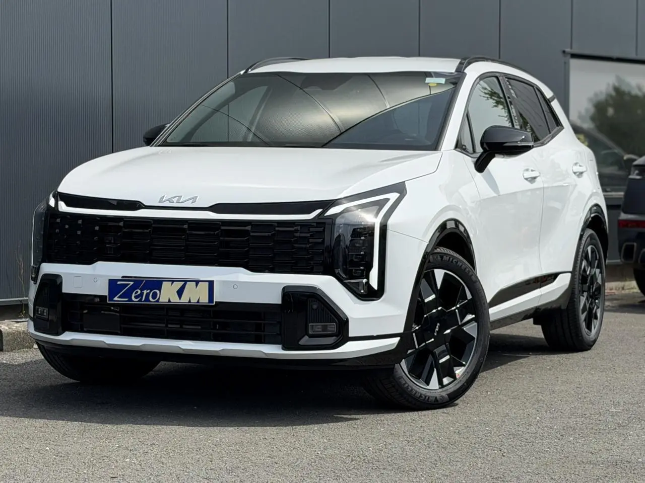 KIA SPORTAGE blanc vue 3/4 avant avec calandre noire et jantes alliage noires distinctives.