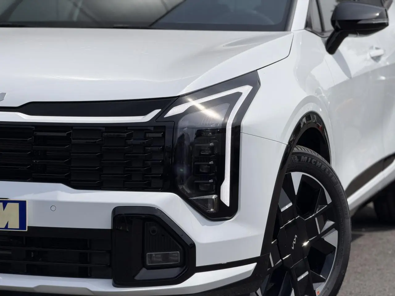 Gros plan sur l'avant droit du KIA Sportage blanc 2026, mettant en valeur le phare LED et la jante alliage noire.