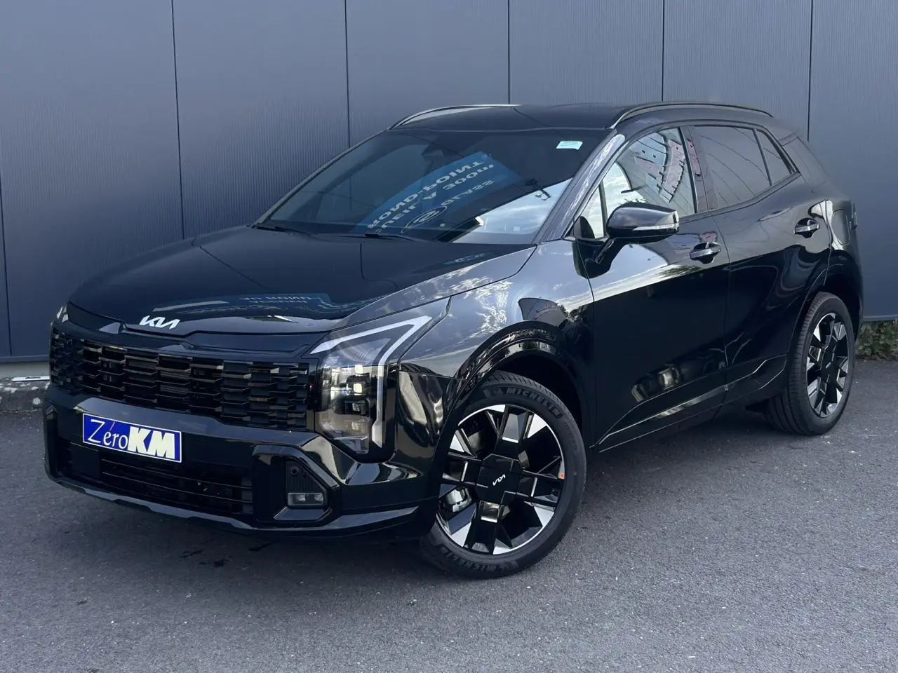 KIA Sportage noir métallisé en 3/4 avant droit, avec calandre noire et jantes alliage 19 pouces distinctives.