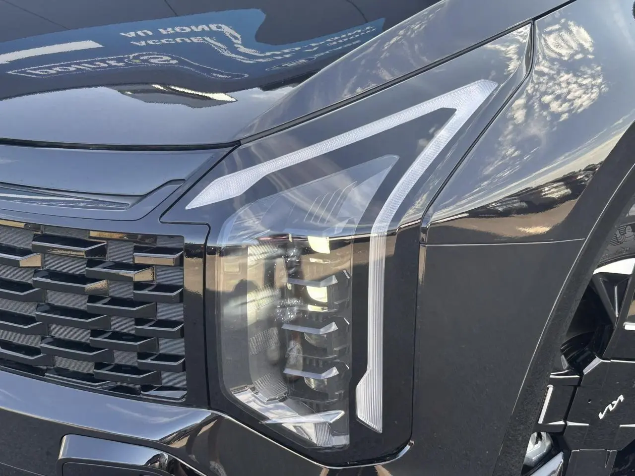 Gros plan sur le phare avant droit noir métallisé du KIA SPORTAGE 2026 avec calandre et jante alliage visibles.