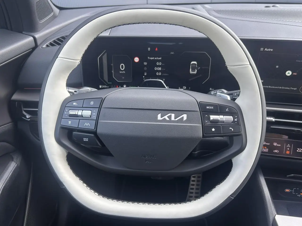 Vue rapprochée du volant bi-ton clair et noir du KIA SPORTAGE 2026 avec tableau de bord digital en arrière-plan.