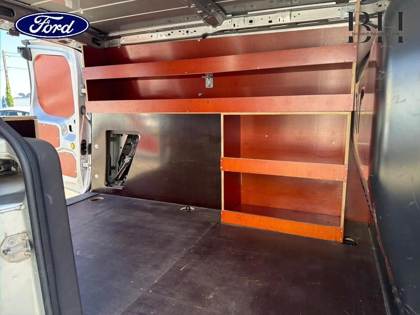 Vue intérieure arrière du Ford Transit Connect gris lunaire, montrant l’espace de chargement avec étagères en bois intégrées.