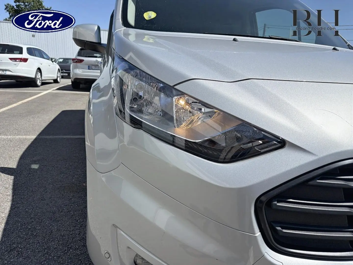 Gros plan sur l'avant droit du Ford Transit Connect gris lunaire métallisé, mettant en valeur le phare et la calandre.