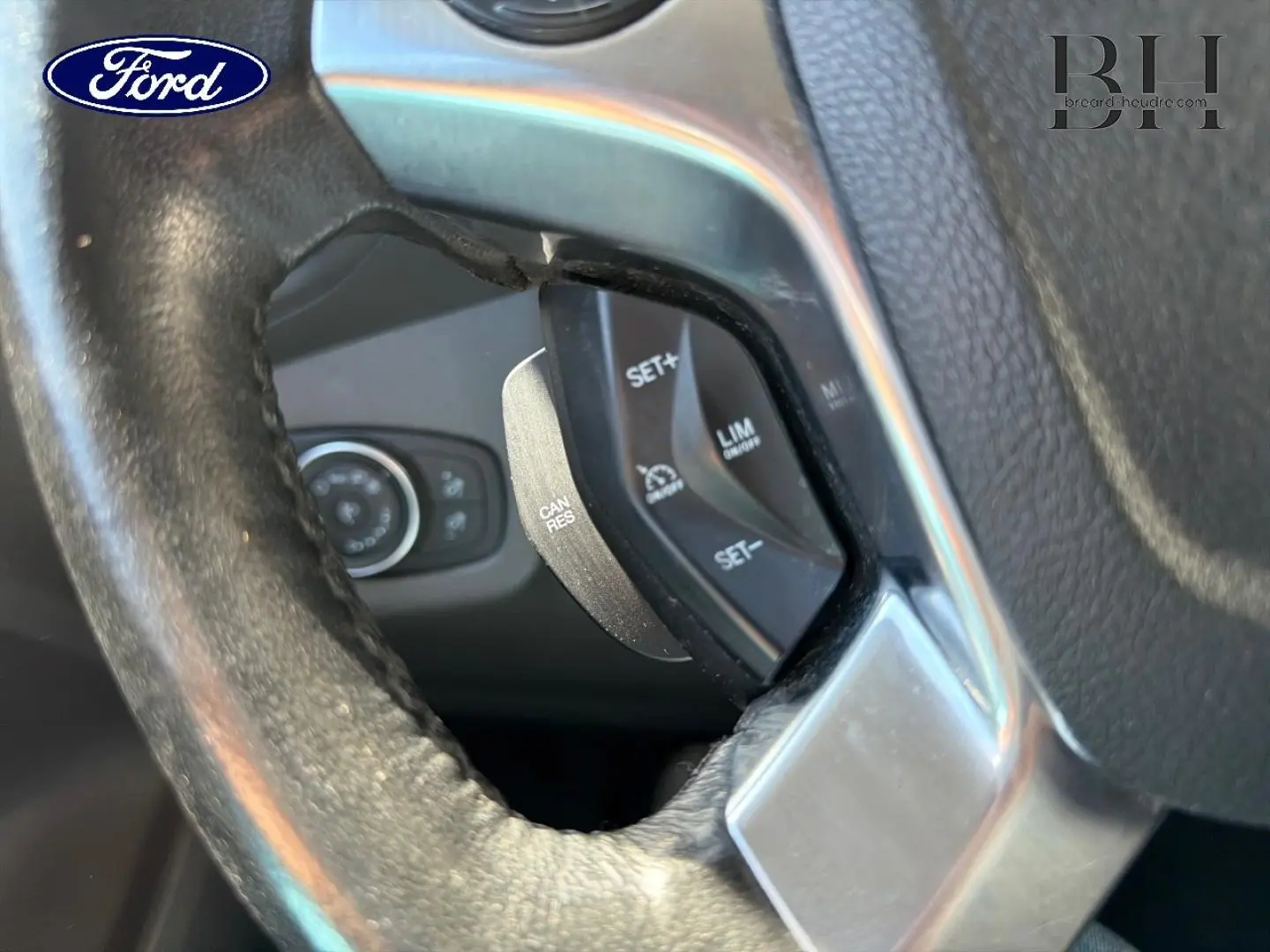 Gros plan sur les commandes de régulateur de vitesse au volant en cuir du Ford Transit Connect gris lunaire.