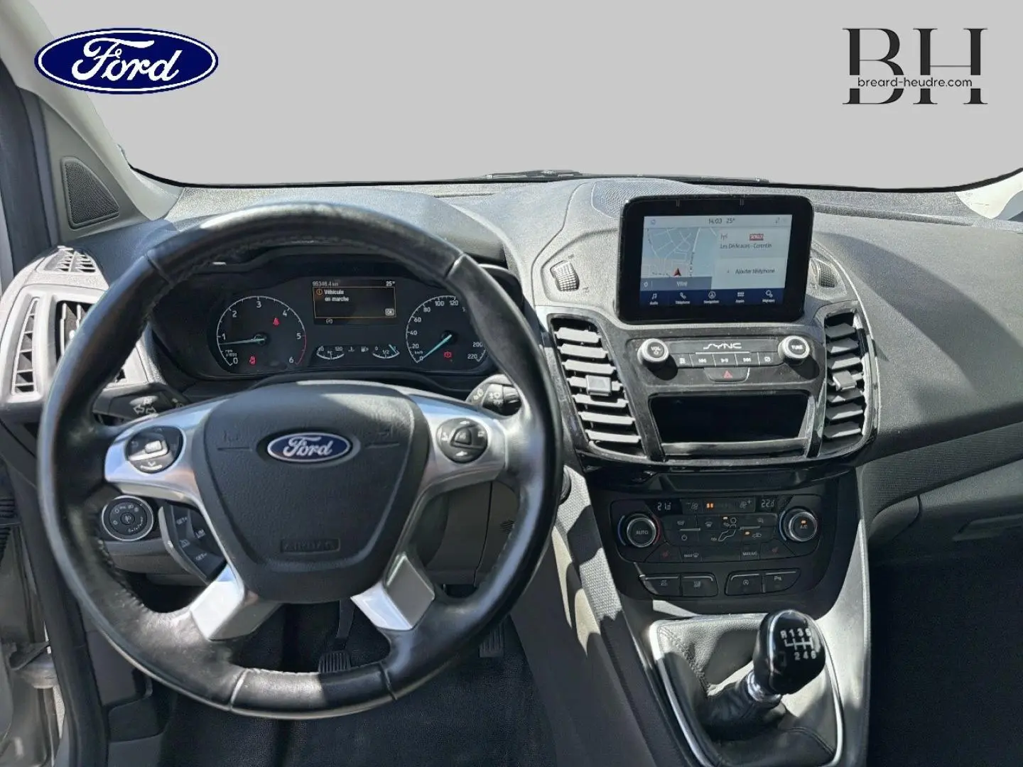 Vue intérieure centrée sur le volant et la console centrale du Ford Transit Connect gris lunaire avec écran tactile et levier manuel.