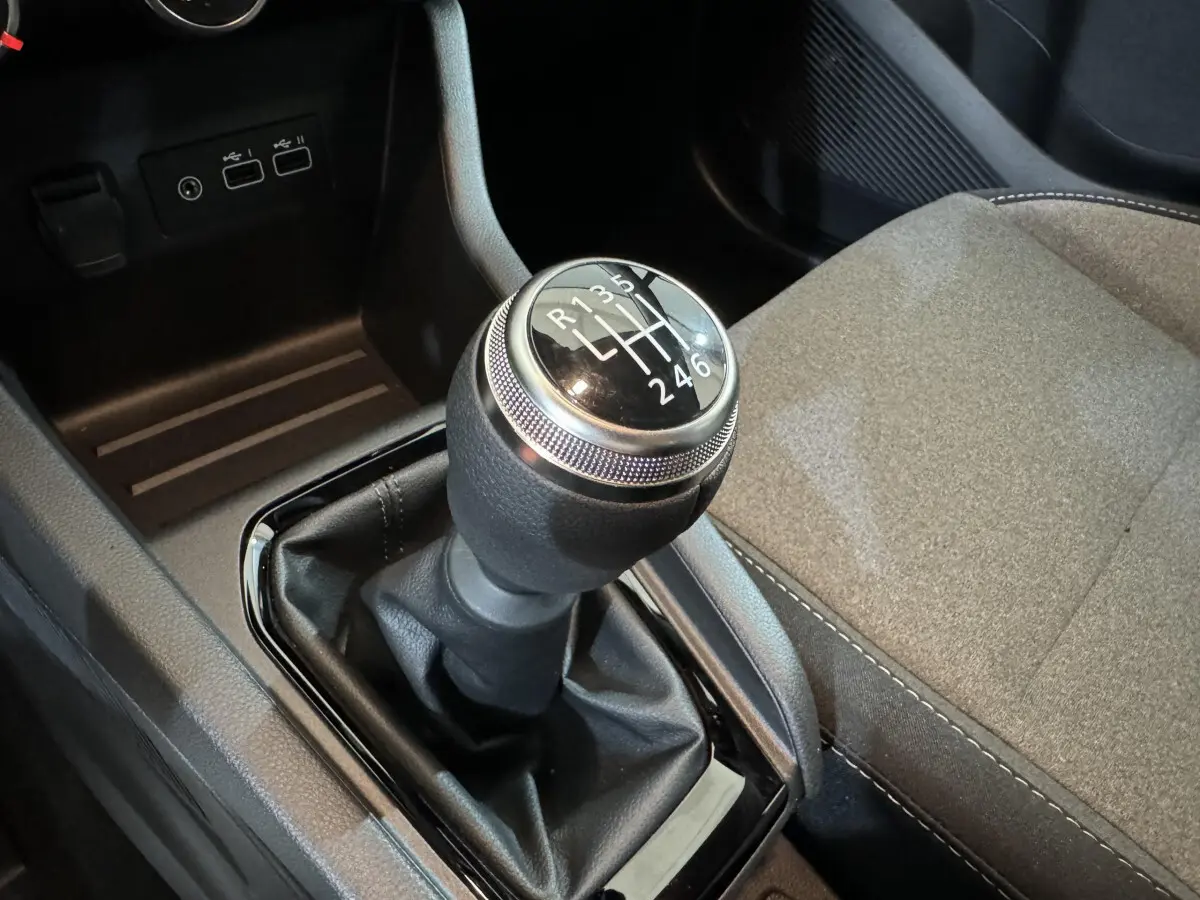 Gros plan sur le levier de vitesses manuel noir et argenté, avec siège tissu gris clair à côté dans une Renault Clio 2025.