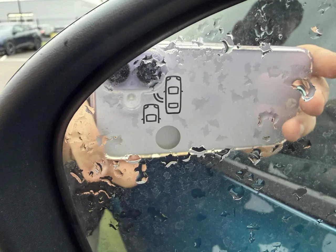 Rétroviseur côté gauche de Renault Arkana bleu Zanzibar, avec icône d'alerte d'angle mort visible sous pluie.