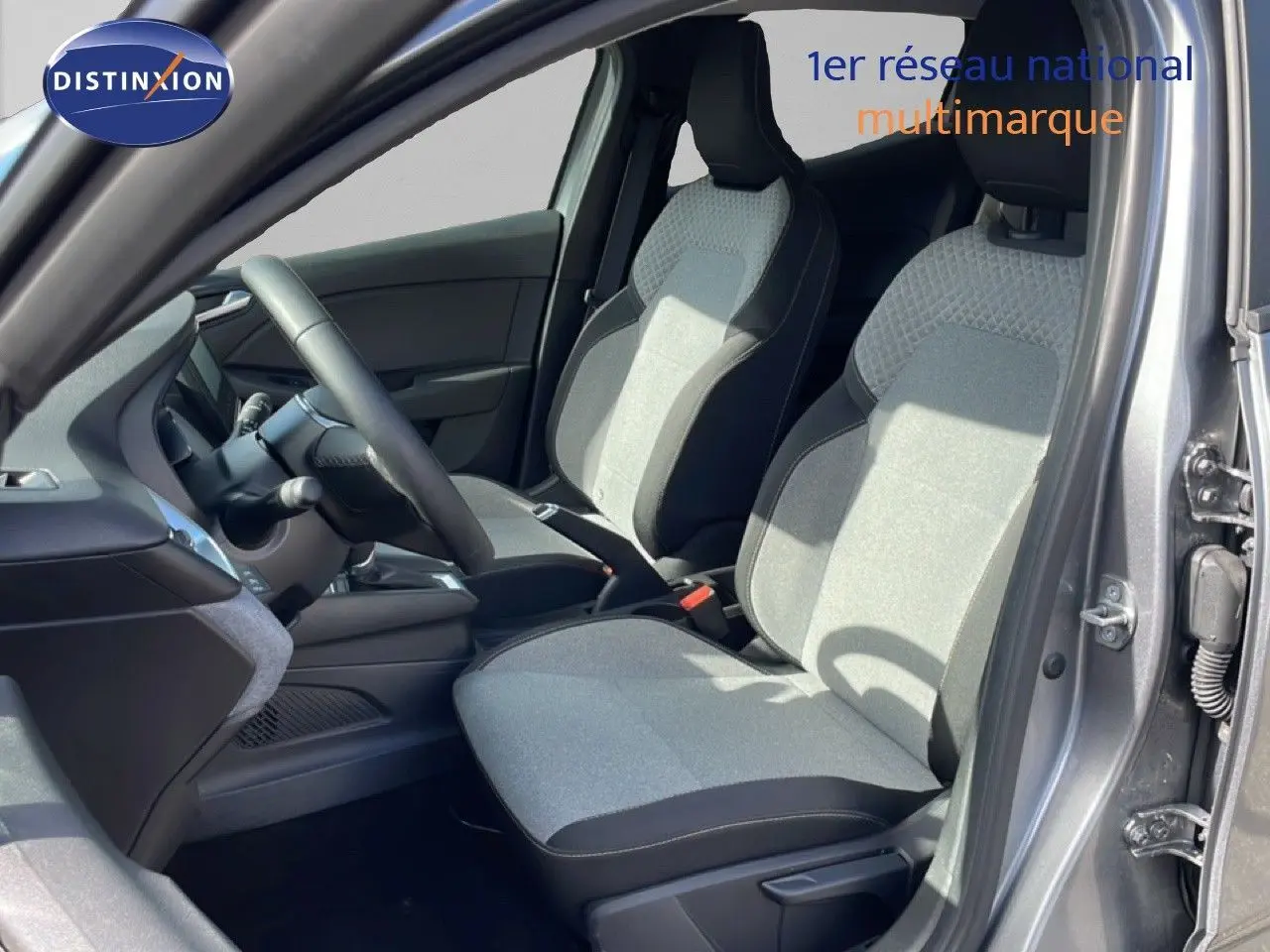Vue intérieure côté conducteur de la Renault Clio 2025 gris schiste métal, sièges tissu bicolore et volant cuir multifonction.