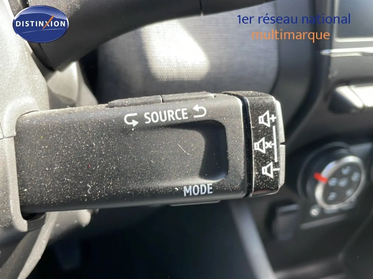 Gros plan sur la commande au volant Renault Clio 2025, bouton source et mode en plastique noir texturé.