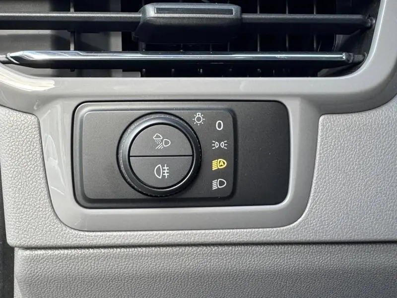 Gros plan sur le bouton de commande des phares dans l'habitacle gris clair du Volkswagen Transporter FGN 2025.