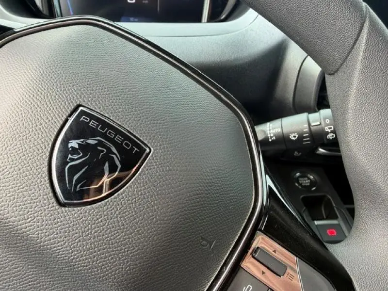Gros plan sur le volant noir avec logo Peugeot du Partner XL 2025, montrant les commandes intégrées et le commodo droit.