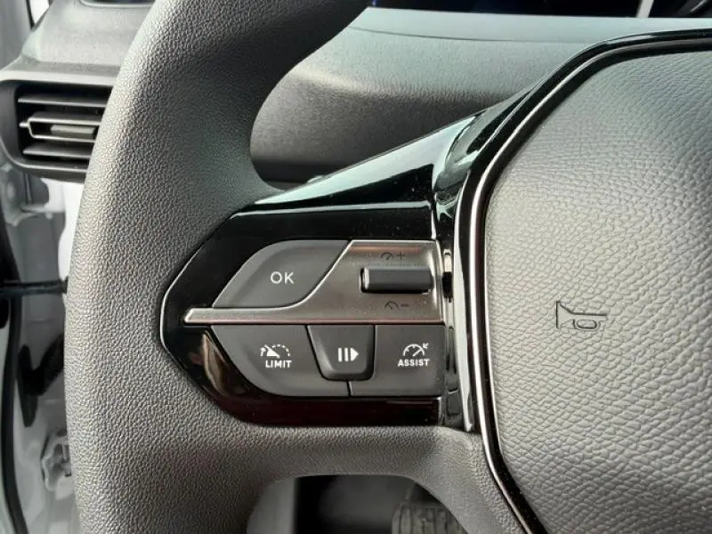 Gros plan sur les commandes au volant à gauche du Peugeot Partner XL blanc Icy, avec boutons multifonctions et finition noire brillante.