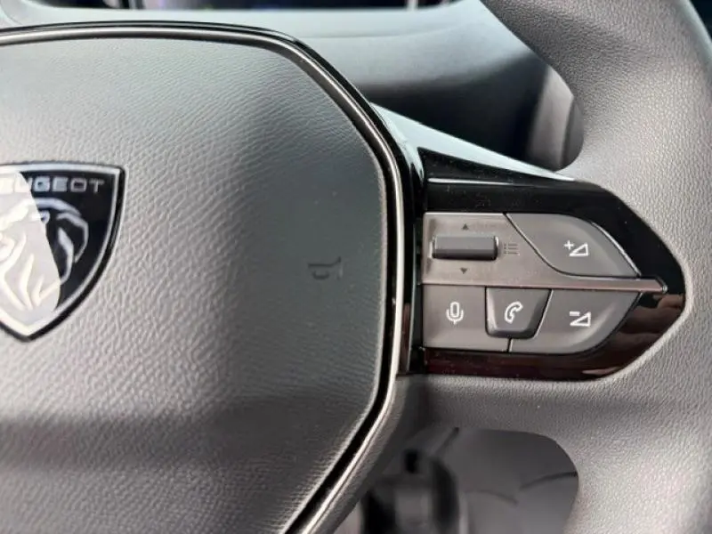 Gros plan sur les commandes multifonctions à droite du volant gris du Peugeot Partner XL 2025, avec logo visible.