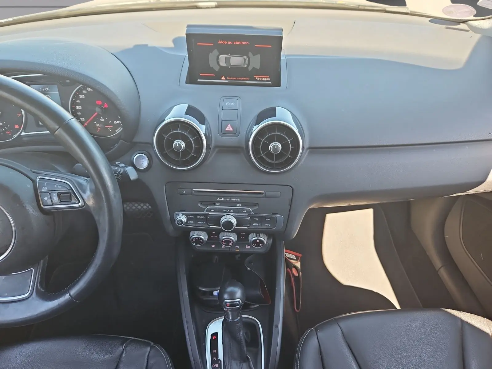 Vue intérieure avant de l’Audi A1 Sportback 2016 noire, mettant en valeur le tableau de bord et la console centrale avec écran tactile.