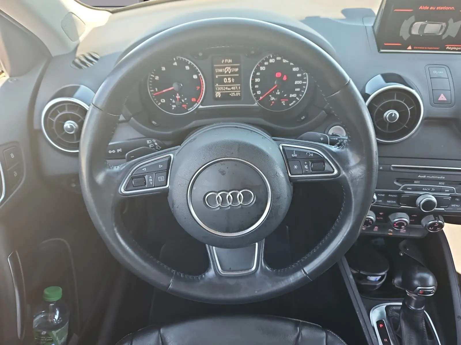 Vue centrée sur le volant sport noir et le tableau de bord de l'Audi A1 Sportback 2016 avec écran tactile et commandes intégrées.