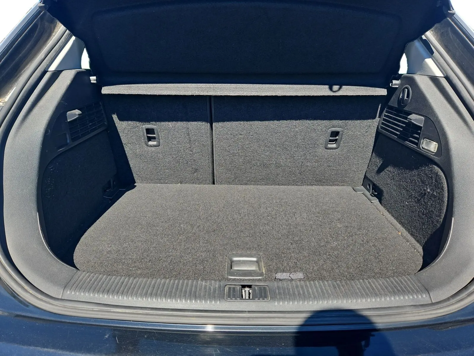 Coffre ouvert vu de l'arrière d'une Audi A1 Sportback noire, montrant un espace de chargement propre et bien fini.