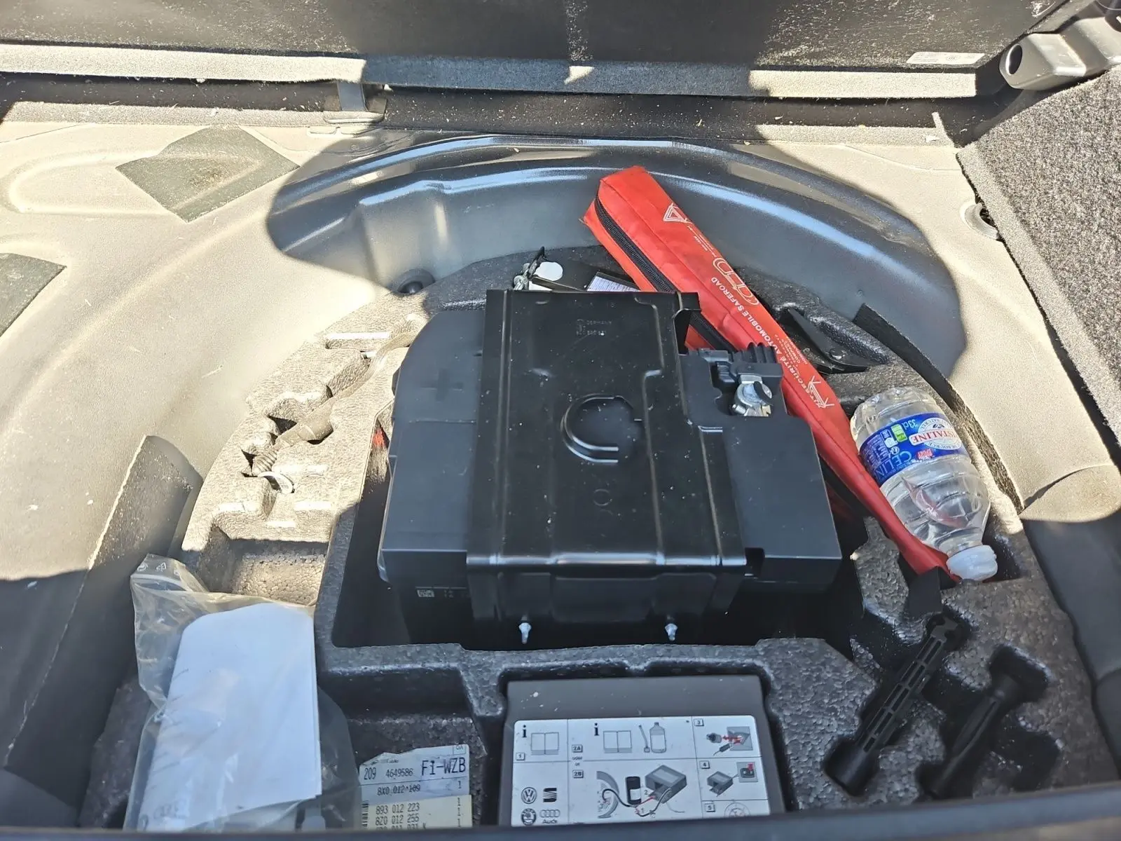Vue rapprochée du coffre d'une Audi A1 noire, montrant la batterie et le kit anti-crevaison rangés sous le plancher.