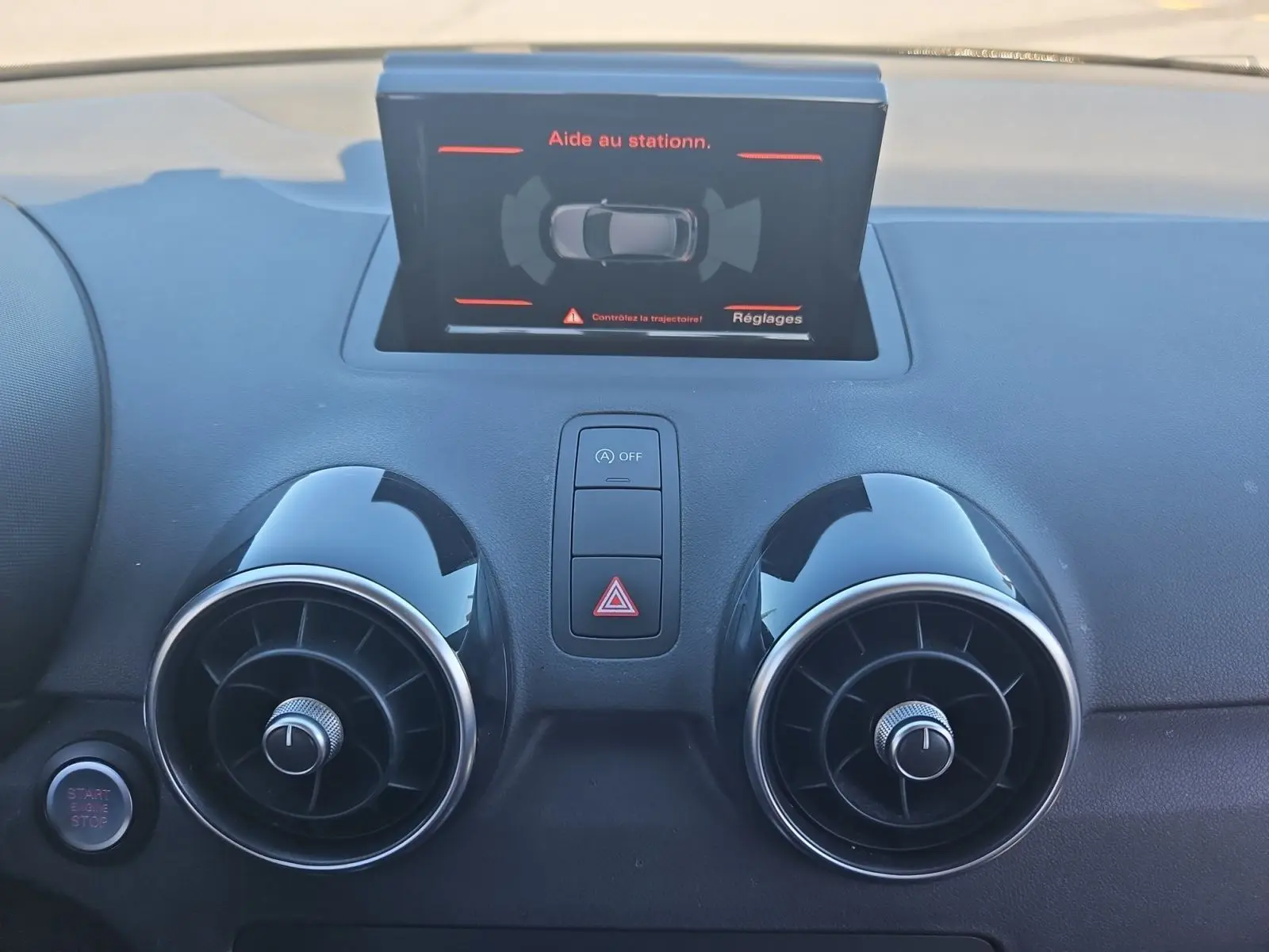 Vue rapprochée du tableau de bord noir de l'Audi A1 Sportback 2016 avec écran d'aide au stationnement et aérateurs ronds.