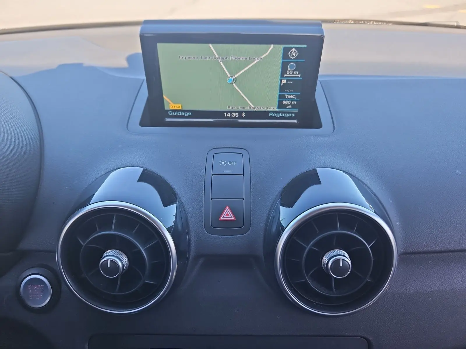 Vue rapprochée du tableau de bord noir d'une Audi A1 Sportback 2016, avec écran GPS et aérateurs ronds chromés.