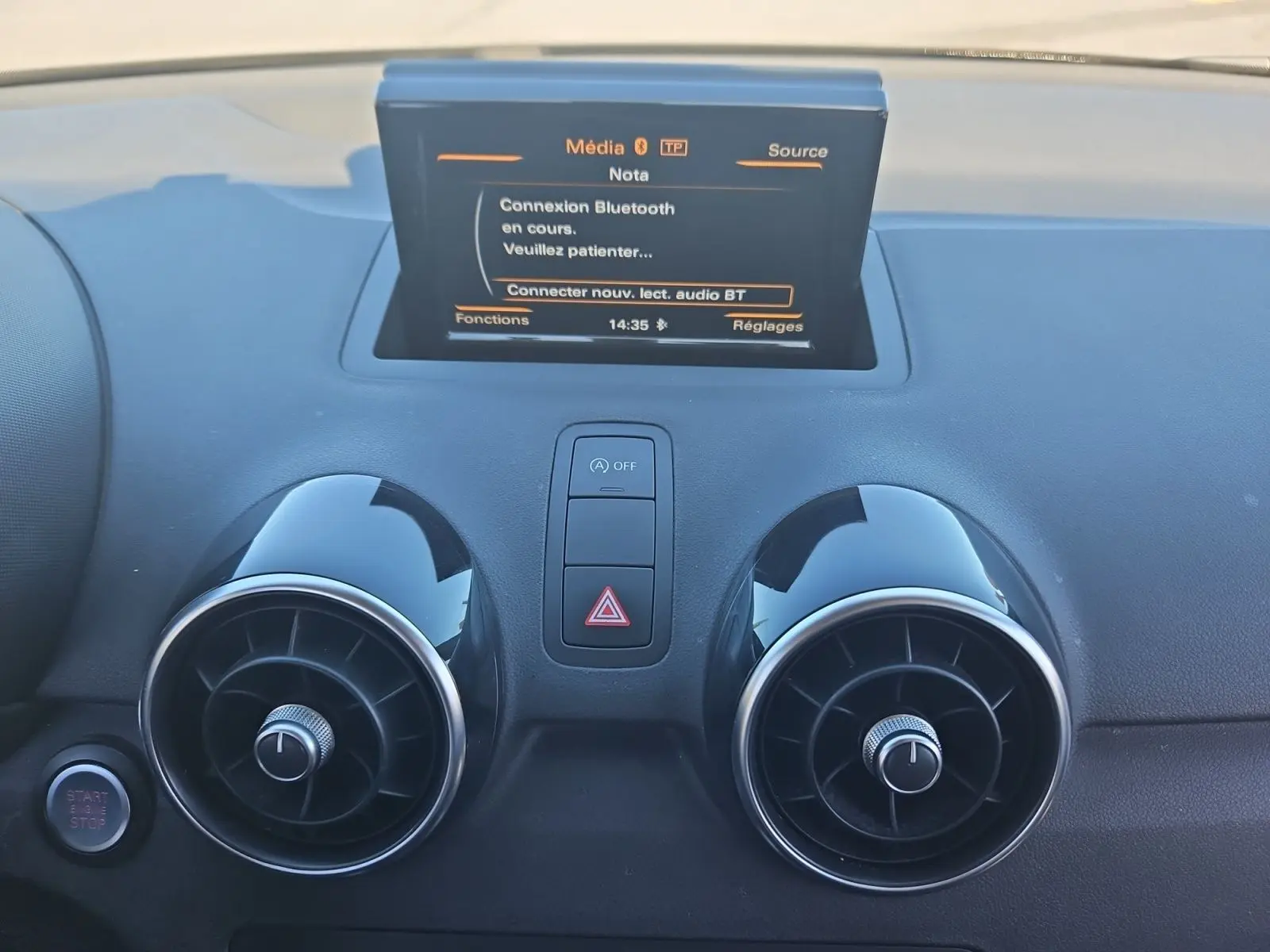 Vue rapprochée du tableau de bord noir de l’Audi A1 avec écran tactile et aérateurs ronds chromés.