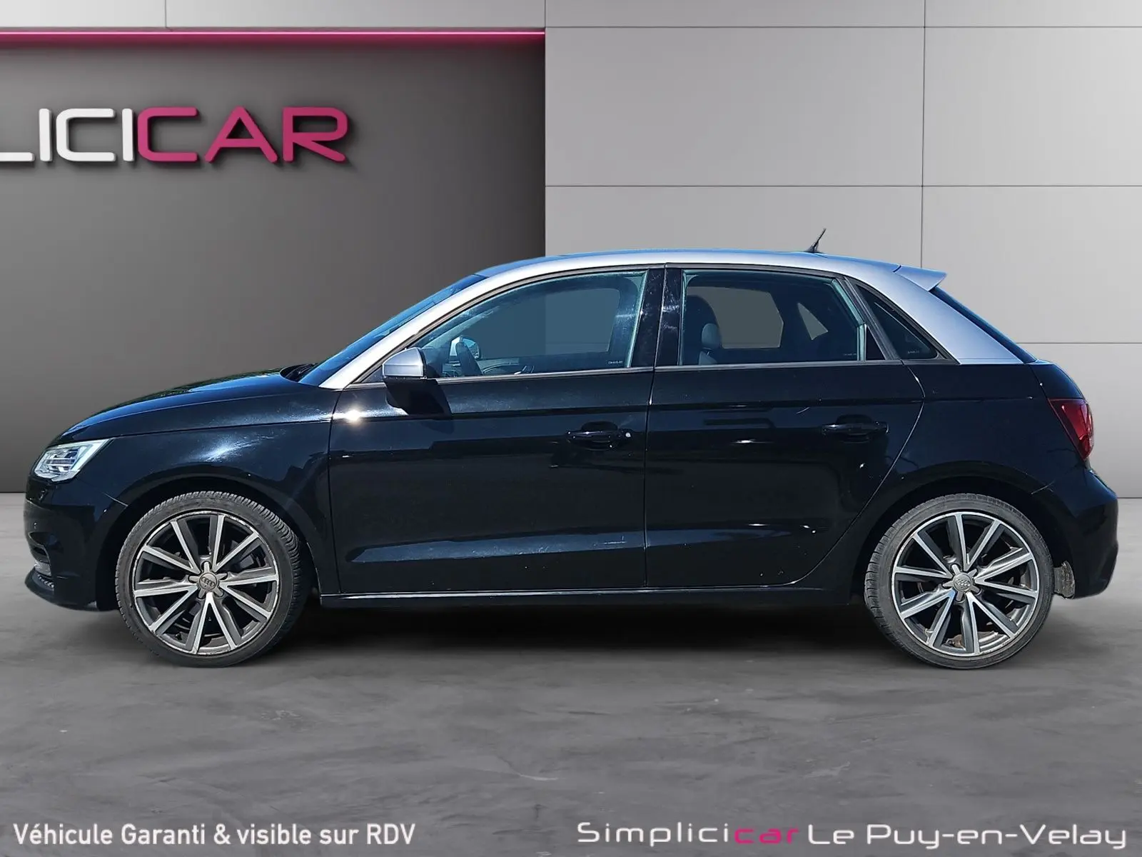 Vue de profil côté gauche d'une Audi A1 Sportback noire avec toit argenté et jantes alliage 17 pouces.
