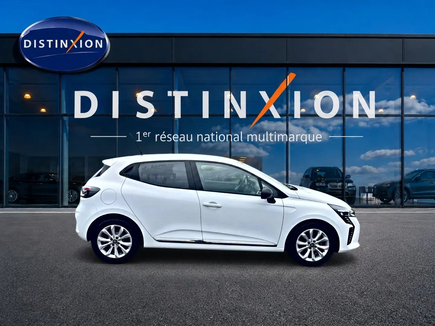 Profil droit d'une Renault Clio V blanche 2025, avec jantes alliage et rétroviseurs noirs, devant une vitrine Distinxion.