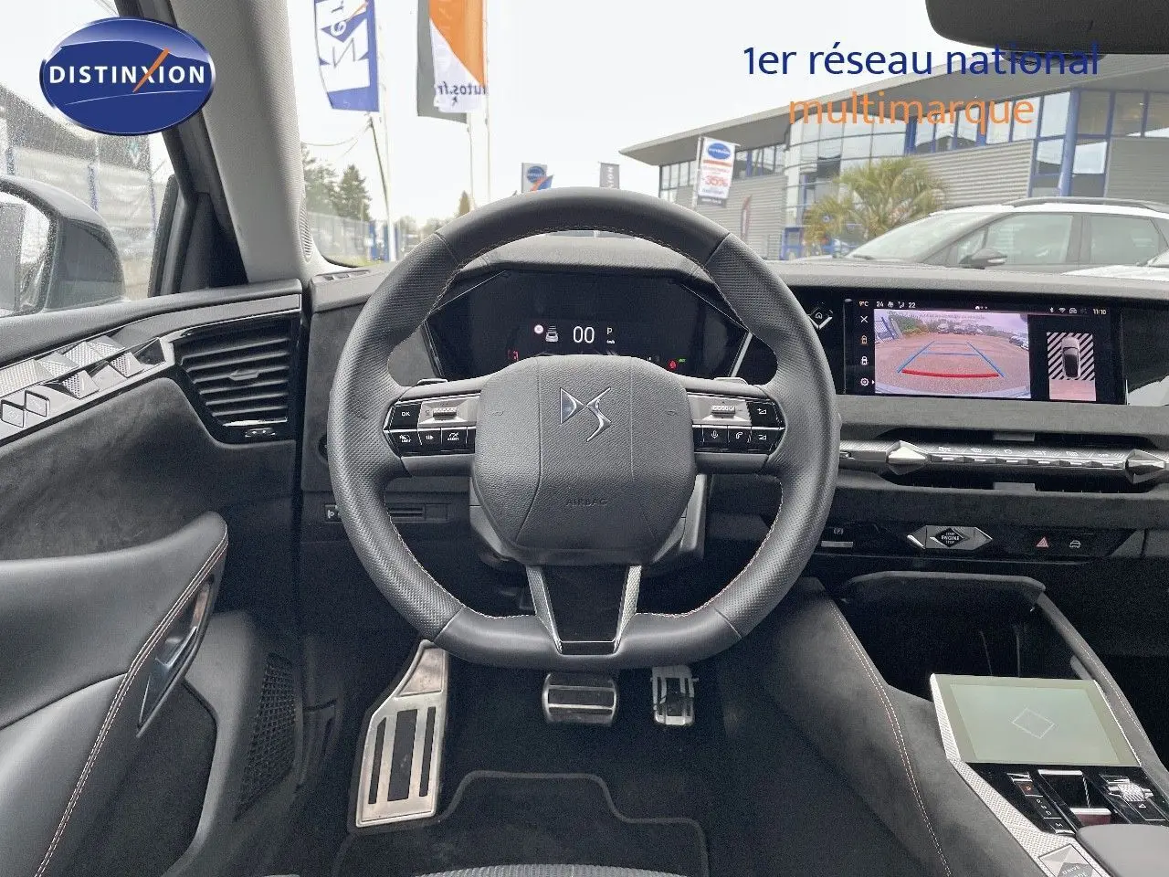 Vue intérieure centrée sur le volant cuir noir du DS4 2024, avec tableau de bord digital et écran multimédia affichant la caméra de recul.