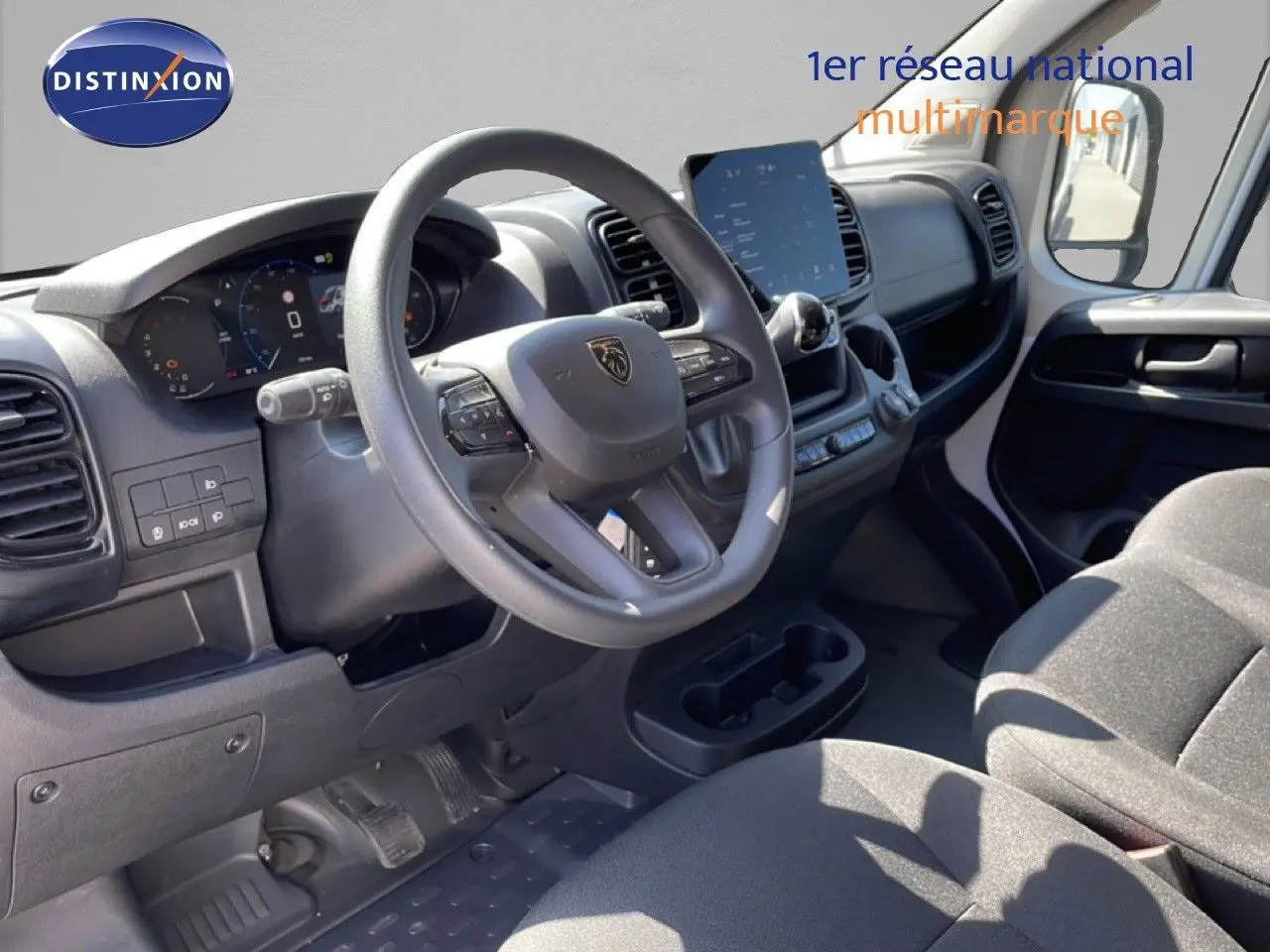 Vue intérieure côté conducteur du Peugeot Boxer Fourgon 2025, montrant le volant, tableau de bord numérique et sièges en tissu noir.