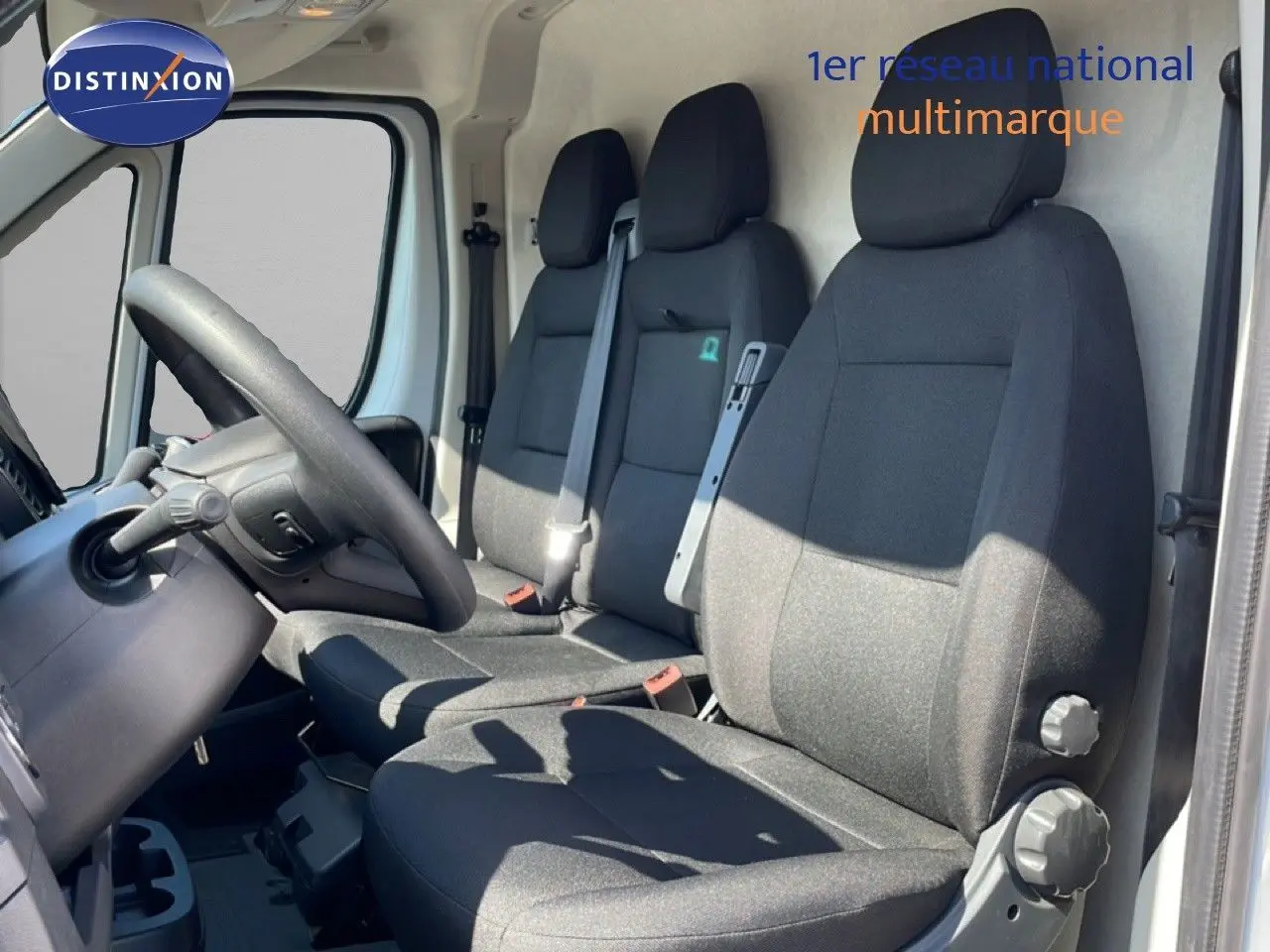 Vue intérieure côté conducteur du Peugeot Boxer Fourgon 2025, sièges tissu noir et volant visible, porte ouverte côté gauche.