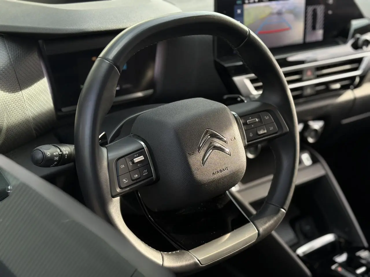 Gros plan sur le volant cuir noir du Citroën C4 X 2024 avec commandes intégrées et tableau de bord moderne en arrière-plan.