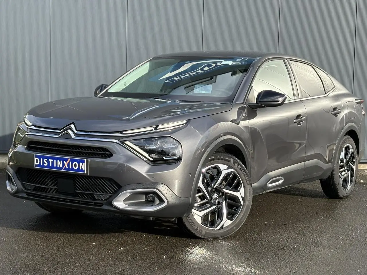 Citroën C4 X gris Platinium en 3/4 avant droit, avec jantes alliage et signature lumineuse LED distinctive.