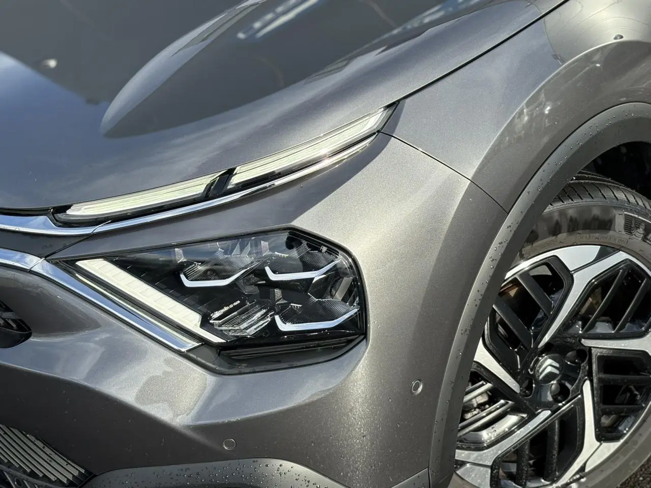 Gros plan sur l'avant droit gris Platinium du Citroën C4 X 2024, mettant en valeur son phare LED et jante alliage diamantée.