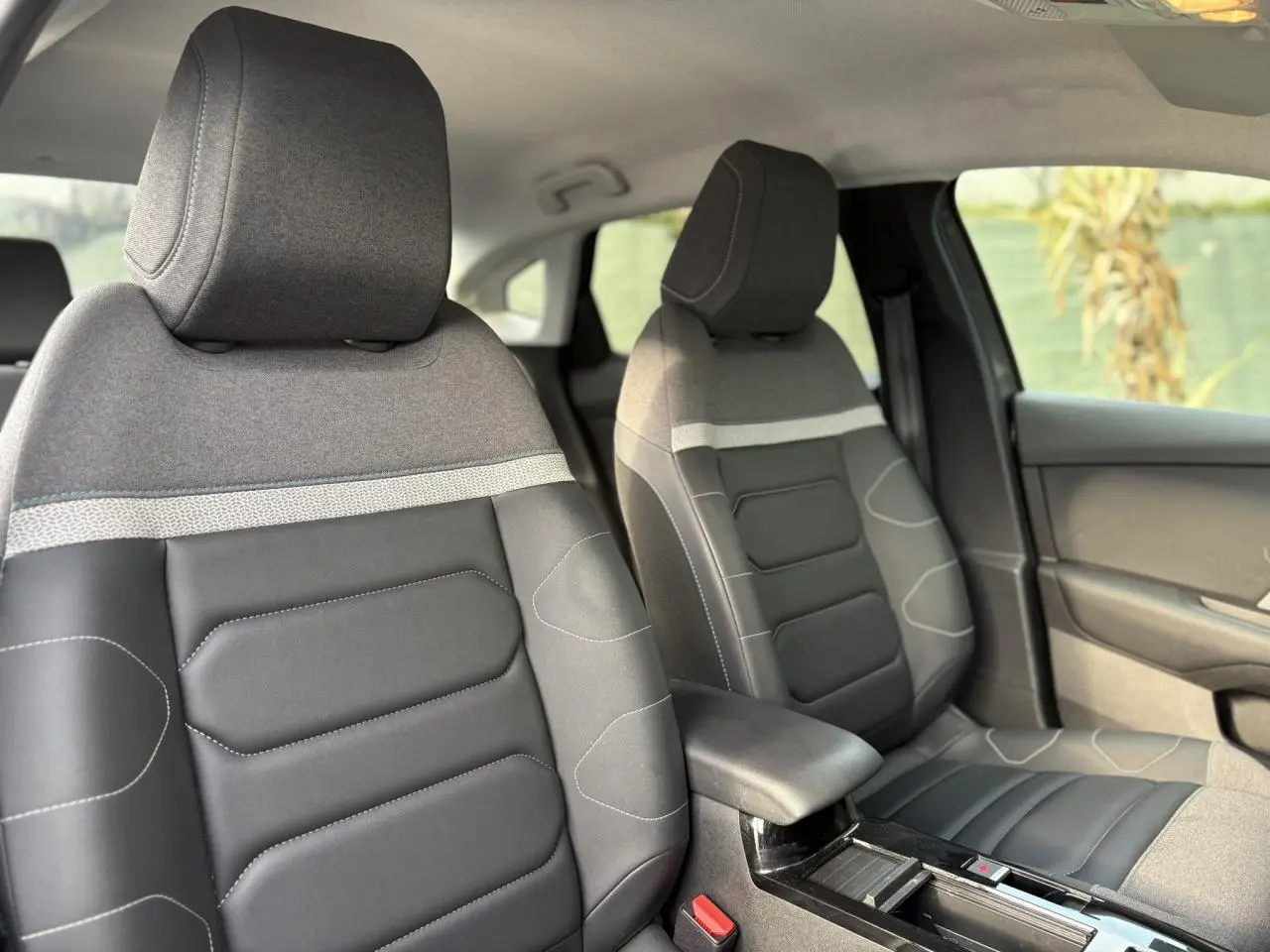 Vue intérieure des sièges avant gris et noirs en tissu et toile enduite du Citroën C4 X 2024, avec accoudoir central.