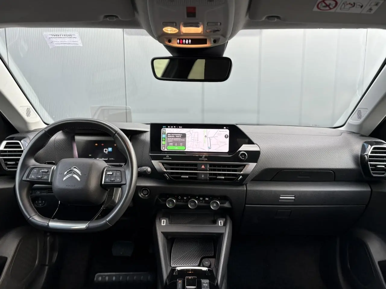 Vue frontale de l’intérieur du Citroën C4 X 2024, tableau de bord noir avec écran tactile et volant cuir.
