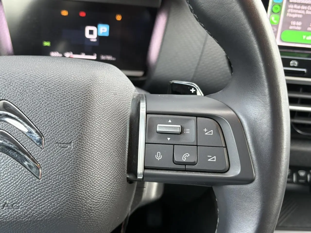 Gros plan sur le côté gauche du volant noir de la Citroën C4 X 2024 avec commandes audio et palettes au volant.