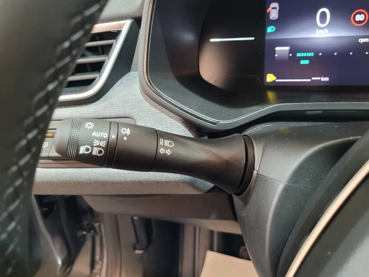 Gros plan sur la commande des feux à gauche du volant dans l’habitacle gris foncé de la Renault Clio Evolution Blue dCi 100 2025.