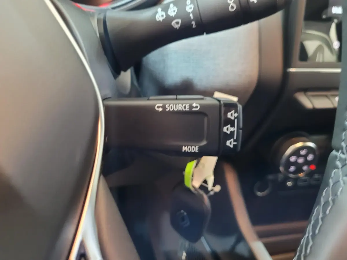 Gros plan sur la commande au volant de la Renault Clio gris foncé, montrant les boutons source et mode.