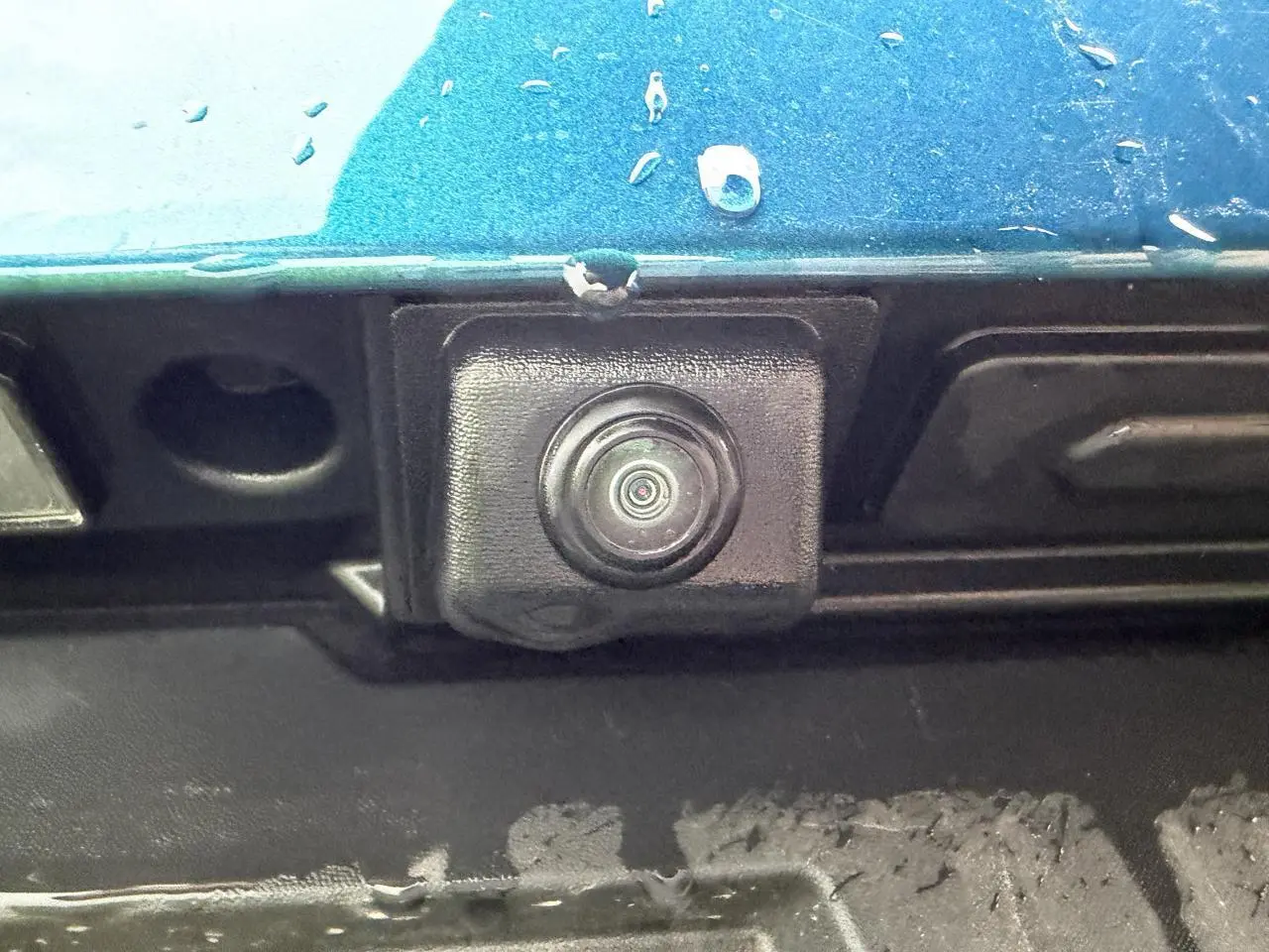 Gros plan sur la caméra de recul noire sous la malle arrière d’une Renault Arkana bleu Zanzibar métallisé.