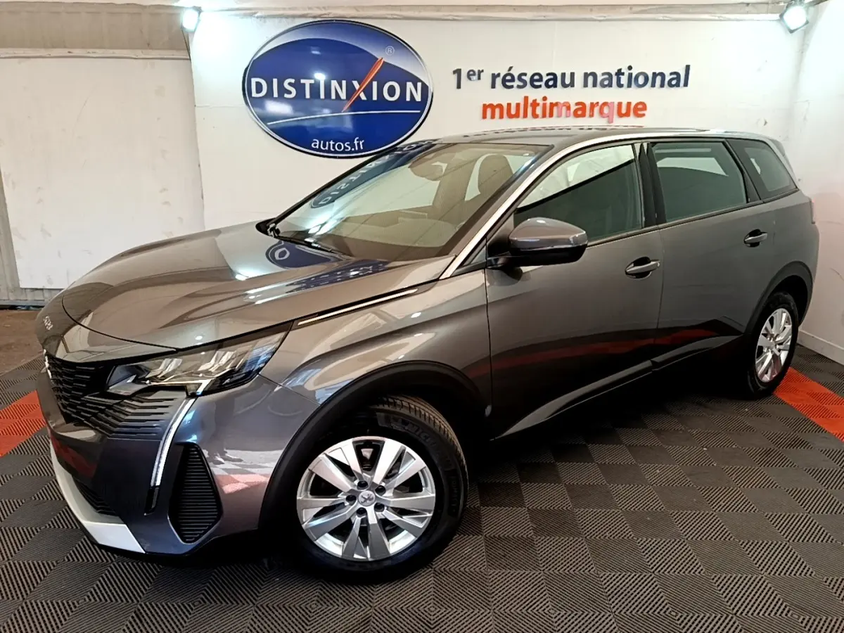 Peugeot 5008 gris clair vue 3/4 avant droit, avec jantes alliage et feux LED, en intérieur showroom.